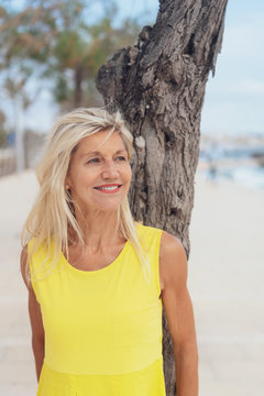 Attractive older woman standing leaning on a tree