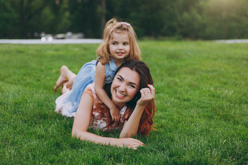 Smiling woman in light dress and little cute child baby girl hug, embrace and lie on grass rest and have fun. Mother, little kid daughter. Mother's Day, love family, parenthood, childhood concept.