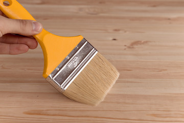 male hand holding a yellow paint brush on wooden background