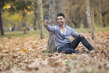 Naklejka na ściany i meble Handsome man in nature taking selfie pictures with his smartphone. Autumn. Copy space