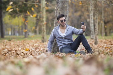 Naklejka na ściany i meble Handsome man in nature taking selfie pictures with his smartphone. Autumn. Copy space