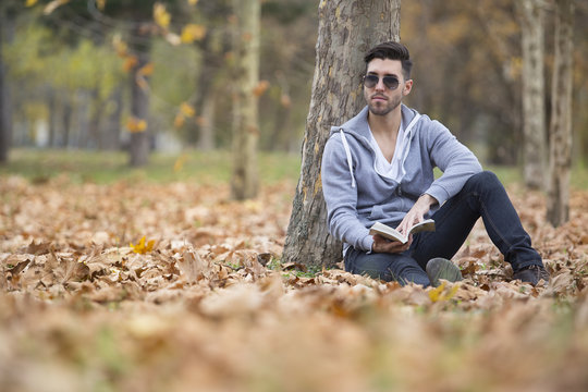 Handsome man in nature reading a book. Autumn leaves. Copy space
