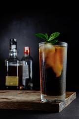 Glass of cola with ice, mint and rosemary on black background