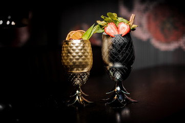 Two cocktails in the steel pineapple form cup with strawberries and mint and berries and orange
