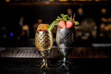 Two fresh cocktails in the pineapple form cups with strawberries and mint and berries and orange