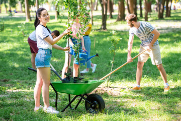 young friends planting new trees and volunteering in park together