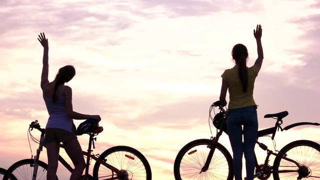 Young friends with bicycles at sunset. Group of young people with bicycles standing at sunset and waving with hands. Enjoying amazing scenery.
