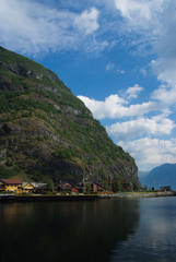 Fototapeta premium Village in Flam, Norway. Country houses at sea shore on mountain landscape. Fjord and mountains on cloudy sky. Vacation and wanderlust. Travelling and discovery