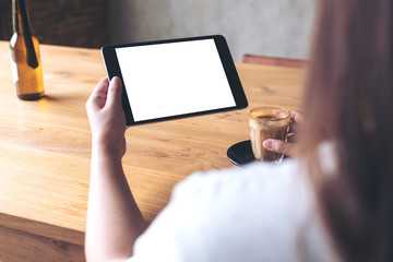 Mockup image of a woman holding black tablet pc with blank white desktop screen while drinking coffee in cafe
