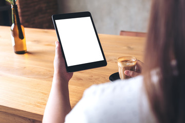 Mockup image of a woman holding black tablet pc with blank white desktop screen while drinking coffee in cafe
