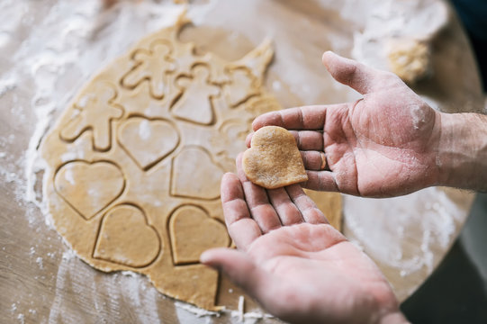 Hands of woman holding unprepared heart-shaped cookie.