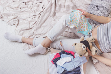 Pregnant woman with a teddy bear and various clothes for a newborn