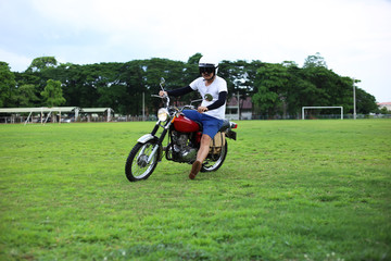 Biker men riding vintage enduro motorcycle on the grass excited and fun lifestyle. Asian rider with classic motorbike.