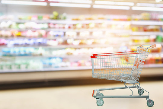 Supermarket product shelves interior blur background with empty shopping cart