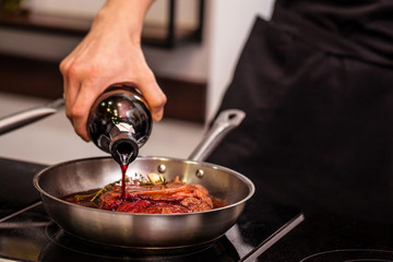 oncept of the correct cooking of meat. The chef prepares, fries a steak of mutton, pork or veal in a frying pan on an induction cooker, with the addition of spices, marinade and wine. Selective focus