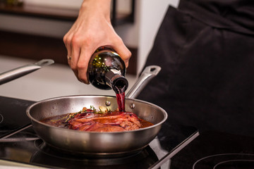 oncept of the correct cooking of meat. The chef prepares, fries a steak of mutton, pork or veal in a frying pan on an induction cooker, with the addition of spices, marinade and wine. Selective focus
