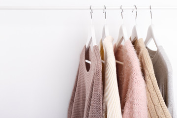 Warm knitted, autumn, winter clothes hanging on a rack, trending concept, pastel colors - obrazy, fototapety, plakaty