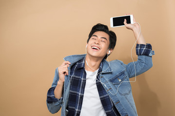 young handsome man on yellow studio background, isolated, listening to music on earphones, holding phone, smiling, happy