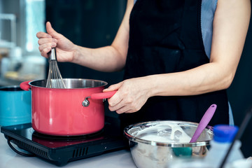 Asian women are mixing the ingredients of a cake in a stainless bowl in her kitchen for weekend party.