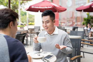 Two young handsome businessmen in casual clothes smiling, talking in coffee shop.