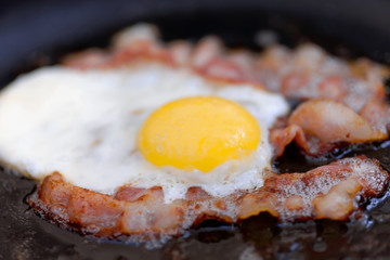Close up fried eggs with bacon on an old iron pan. Shallow depth of field.