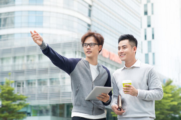 Two smiling male work coworkers outdoors talking together over a digital tablet