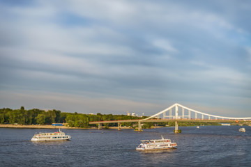 Two observing ships float down the river Dnieper, in windy weather, near the pedestrian bridge on Trukhanov the island, in the capital of Ukraine, the city of Kiev. Created with help tilt-shift lens.