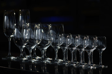 Rows of the empty wineglasses and empty glasses for vodka, stands on a black background. 