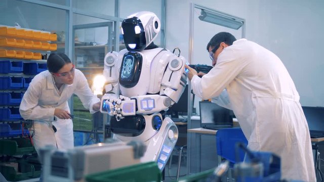 Two workers set a robot to work.