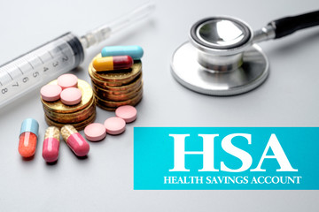 Health Financial concept of HSA Health Savings Account.Stethoscope, syringe, pills and stacked of coins on grey background. Selective focus image.