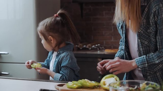 Mother and daughter are trying paprike, while coking in the kitchen, closeup