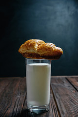 croissant lies on glass of milk on wooden dark table black background