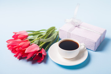 Cup with coffee, bouquet of tulips and pink gift box on a blue background