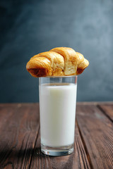 croissant lies on glass of milk on wooden dark table black background