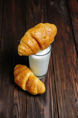 croissant lies on glass of milk on wooden dark table black background