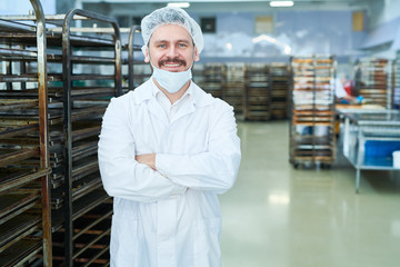 Fototapeta premium Confectionery factory worker standing in white coat with arms crossed smiling and looking at camera. 