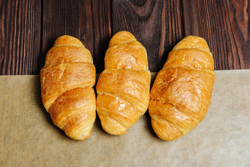 three croissants on wooden table and bakery paper view from above