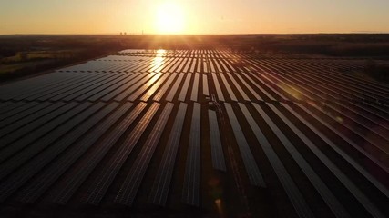 Sunrise over a modern electric solar farm with the sun glistening over the panels as the camera pans over them from the air
