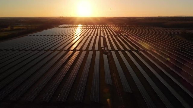 Sunrise over a modern electric solar farm with the sun glistening over the panels as the camera pans over them from the air