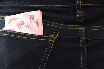 One hundred banknote of Thailand in the back pocket of dark blue jeans.