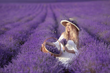 Young blond woman in lavender field. Happy carefree female in a white dress and straw hat enjoying...