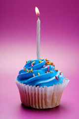 Blue cupcake with candle on color background