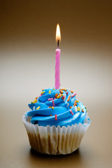 Blue cupcake with candle on color background