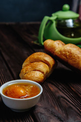 fresh croissants with jam on dark wooden table and tea on background