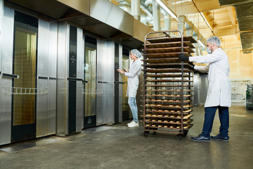 Confectionery factory employees in white coats waiting for elevator to transport trays rack with pastry. © Seventyfour