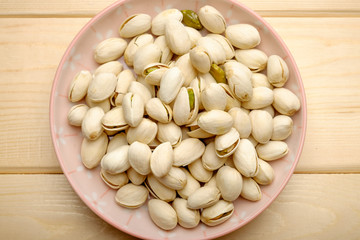 Pistachio nuts on pink ceramic plate and wooden backgroun