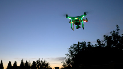 Modern Remote Control Air Drone Fly high with action camera in sunset sky. Cityscape silhouette in the background. Modern technologies. Travel, hobby, inspiration. 