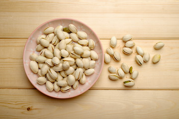 Pistachio nuts on pink ceramic plate and wooden backgroun