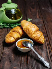 fresh croissants with jam on dark wooden table and tea with rosemary, view from above