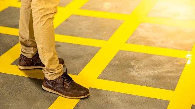 Male legs with trousers pants and brown leather shoes on yellow cross line pattern on concrete floor.